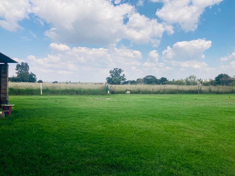 A spacious, well-maintained grassy garden area featuring a wire fence boundary and open views of the surrounding landscape.
