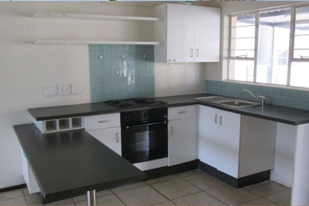 A functional kitchen featuring white cabinetry, dark laminate countertops, a built-in oven, hob, and a double sink with a tiled splashback.