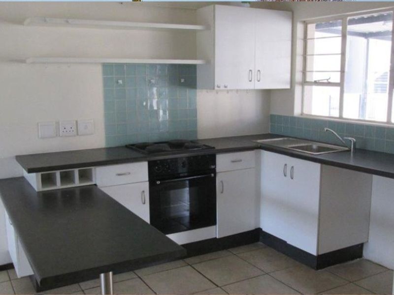 A functional kitchen featuring white cabinetry, dark laminate countertops, a built-in oven, hob, and a double sink with a tiled splashback.