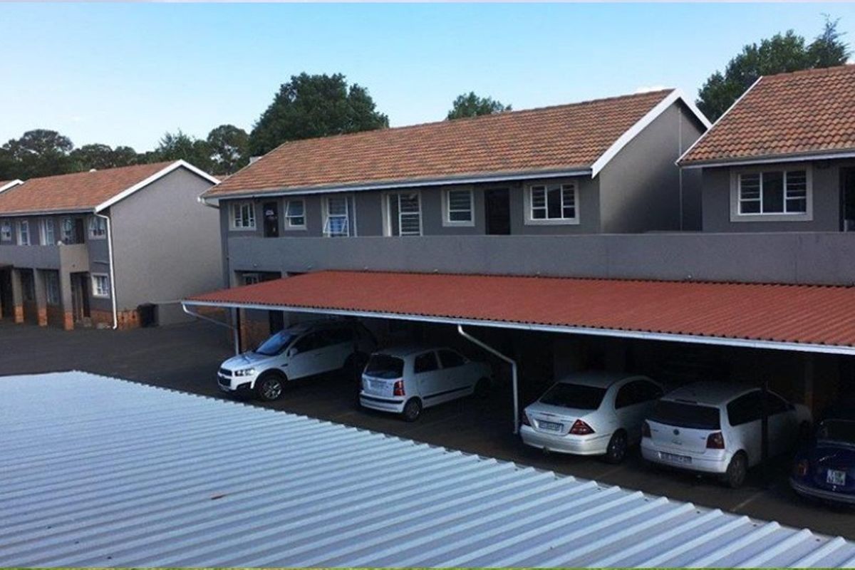 Exterior view of an apartment complex featuring covered parking carports and multi-story residential units with tiled roofing.