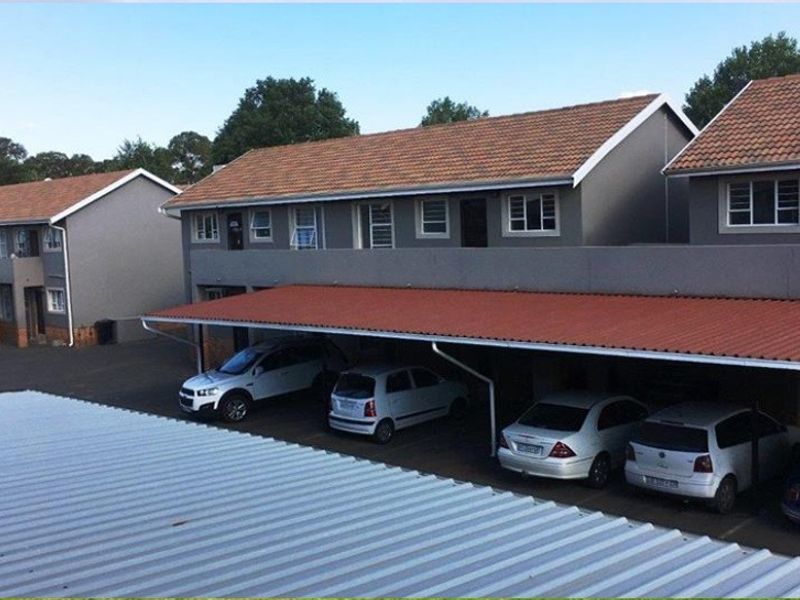 Exterior view of an apartment complex featuring covered parking carports and multi-story residential units with tiled roofing.