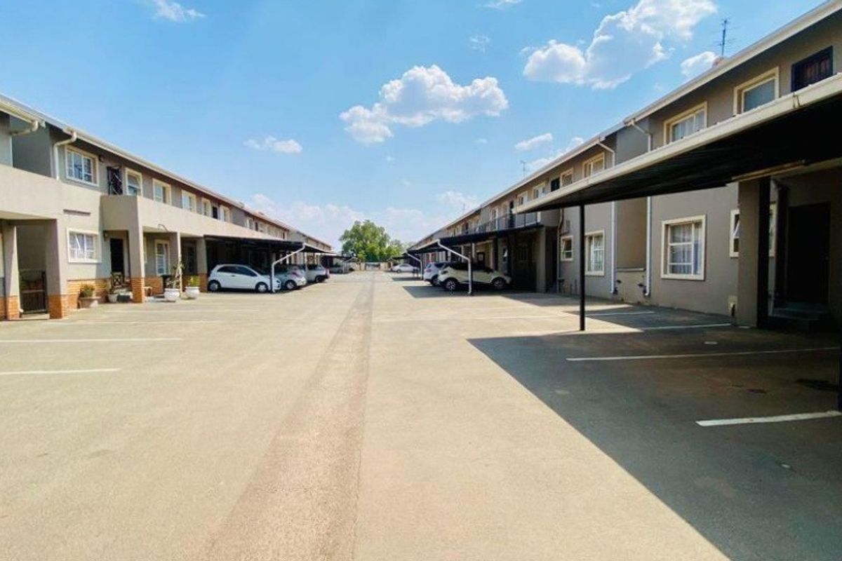 Exterior view of an apartment complex featuring a paved driveway with designated covered parking bays and multi-story residential units.