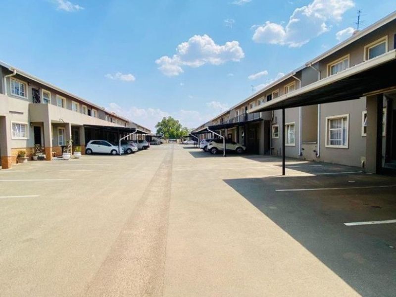 Exterior view of an apartment complex featuring a paved driveway with designated covered parking bays and multi-story residential units.