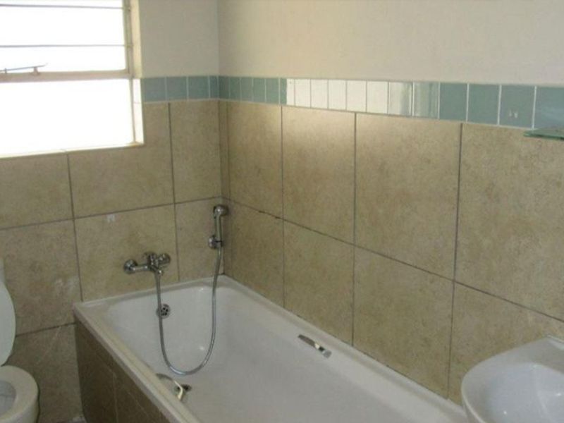 A functional bathroom featuring a bathtub with handheld shower mixer, pedestal basin, and tiled wall finishes.