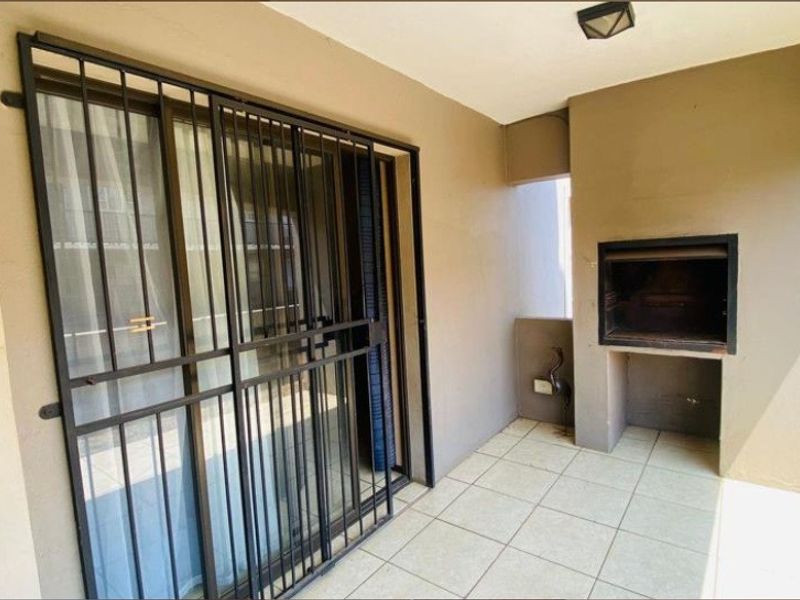 Covered patio area featuring tiled flooring, a built-in braai, and a secure sliding door entrance.