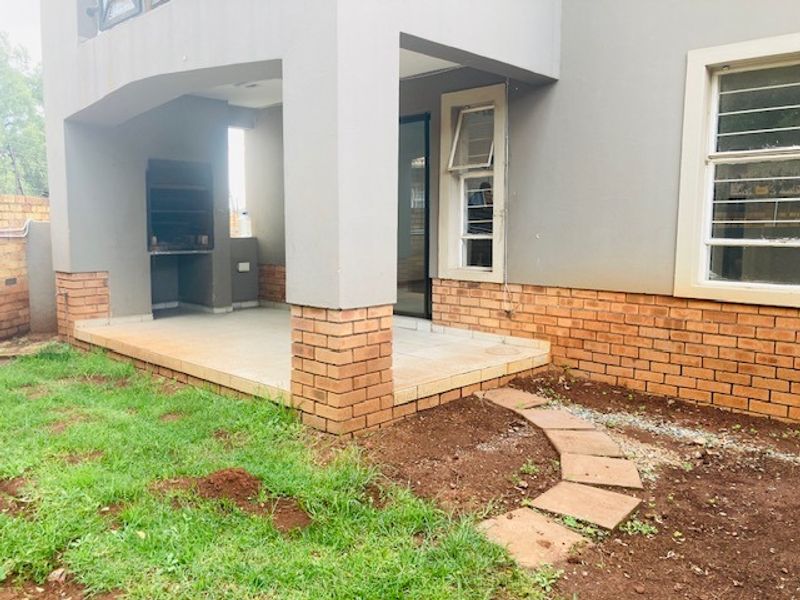 Covered patio area featuring a built-in braai, tiled flooring, and direct access to the garden through a sliding door.