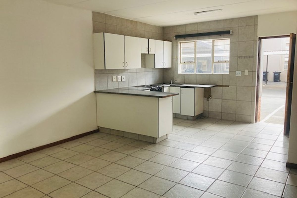 A functional, empty kitchen featuring tiled flooring, built-in cabinetry, a hob, and a tiled backsplash, with direct access to an exterior area.