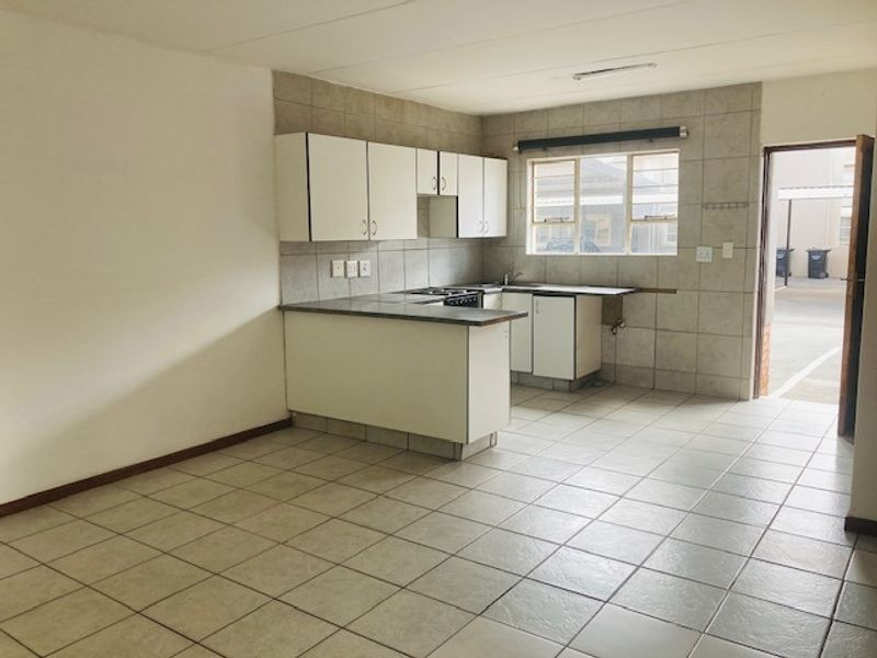 A functional, empty kitchen featuring tiled flooring, built-in cabinetry, a hob, and a tiled backsplash, with direct access to an exterior area.