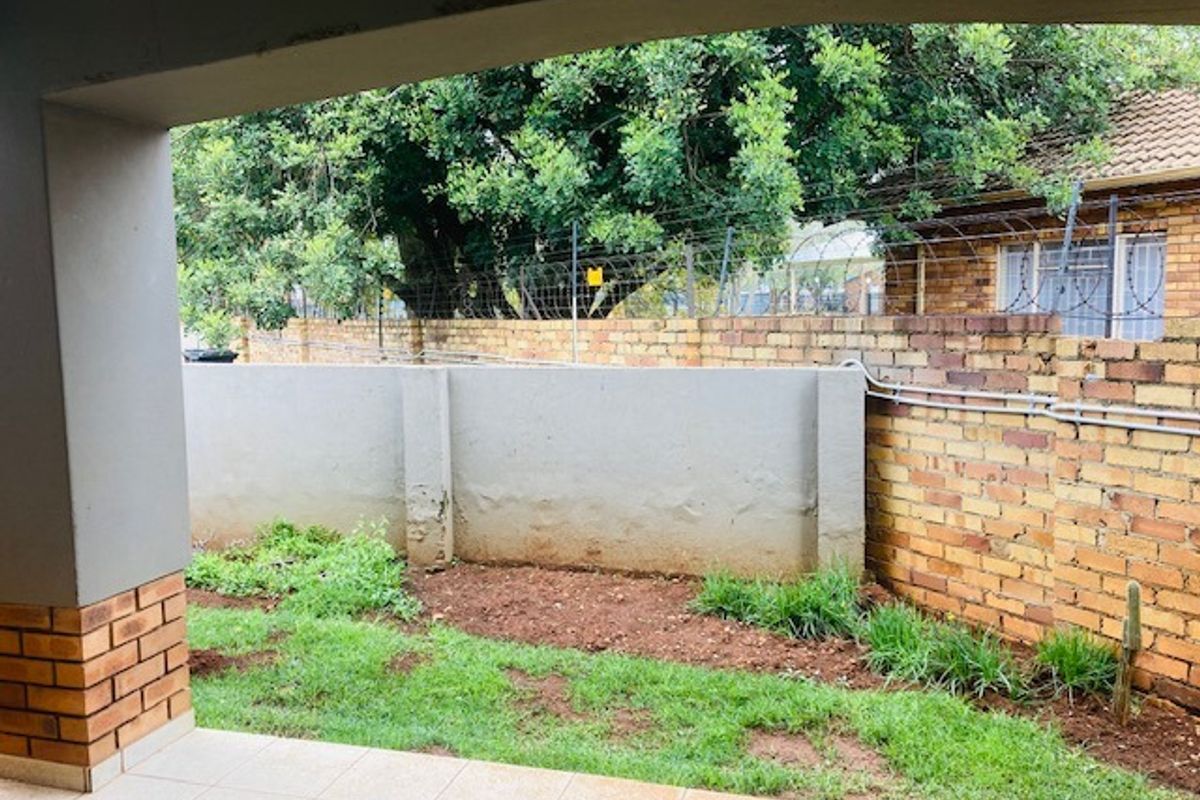 A covered patio area overlooking a small private garden space enclosed by brick boundary walls and security fencing.