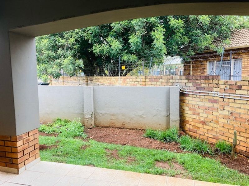 A covered patio area overlooking a small private garden space enclosed by brick boundary walls and security fencing.