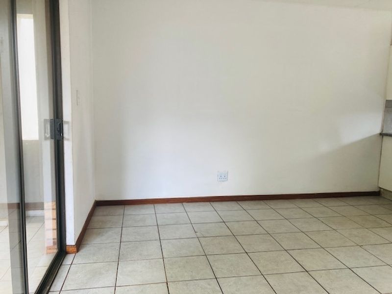An empty open-plan living area featuring neutral ceramic floor tiles, wooden skirting boards, and a sliding glass door leading to an outdoor space.