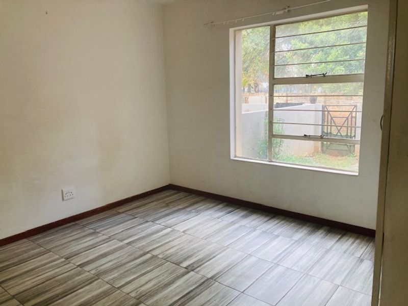 An empty bedroom featuring wood-look tiled flooring, a large window with security bars, and neutral wall finishes.