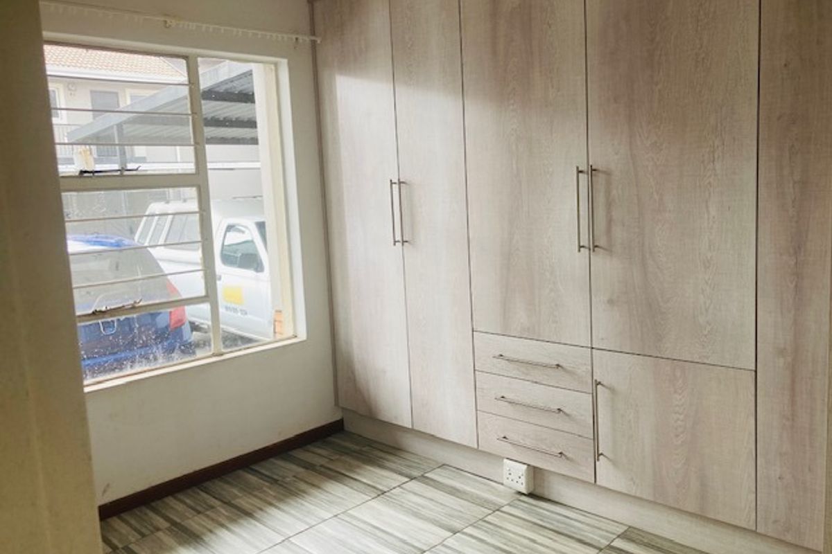A bright bedroom featuring modern light wood-grain built-in cupboards and neutral tiled flooring, offering a clean and functional space.