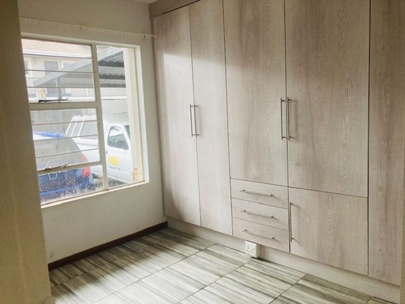 A bright bedroom featuring modern light wood-grain built-in cupboards and neutral tiled flooring, offering a clean and functional space.