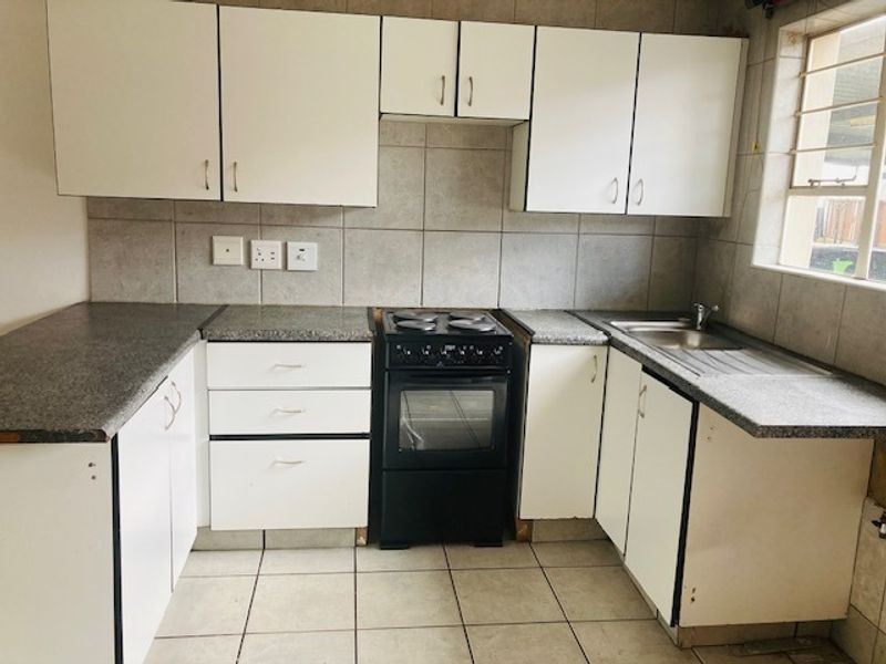 A functional kitchen featuring white cabinetry, laminate countertops, a tiled backsplash, and a freestanding stove, offering potential for modern cosmetic updates.
