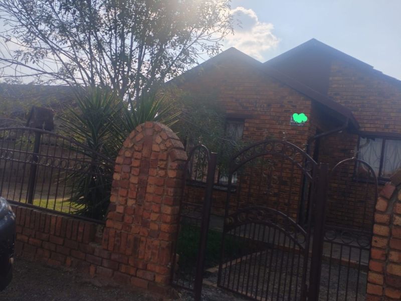Front view of a face brick house featuring a secure wrought iron gate and perimeter walling with established garden elements.