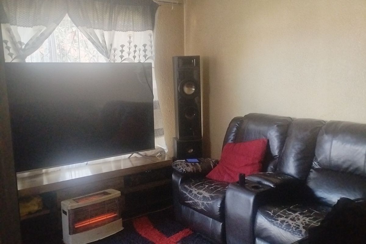 A compact living room featuring a coved ceiling and a window, currently showing signs of wear on the walls and ceiling.