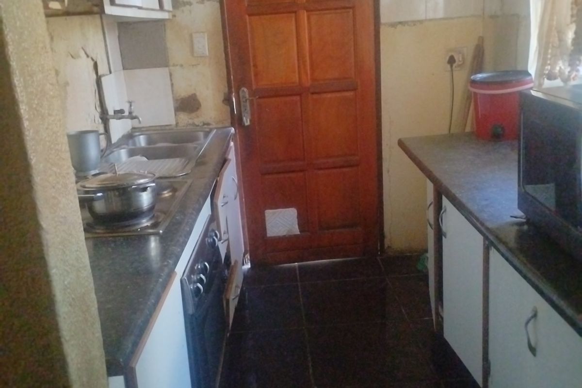 A compact kitchen featuring built-in cabinetry, laminate countertops, and a stainless steel sink, currently requiring significant cosmetic updates and wall repairs.