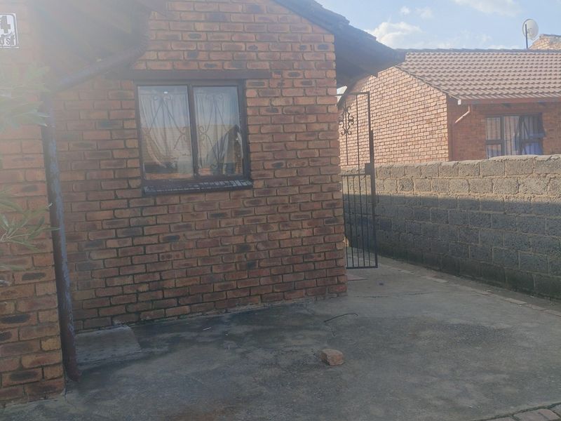 A rear view of a face brick house featuring a concrete patio area, security gate, and surrounding boundary wall.