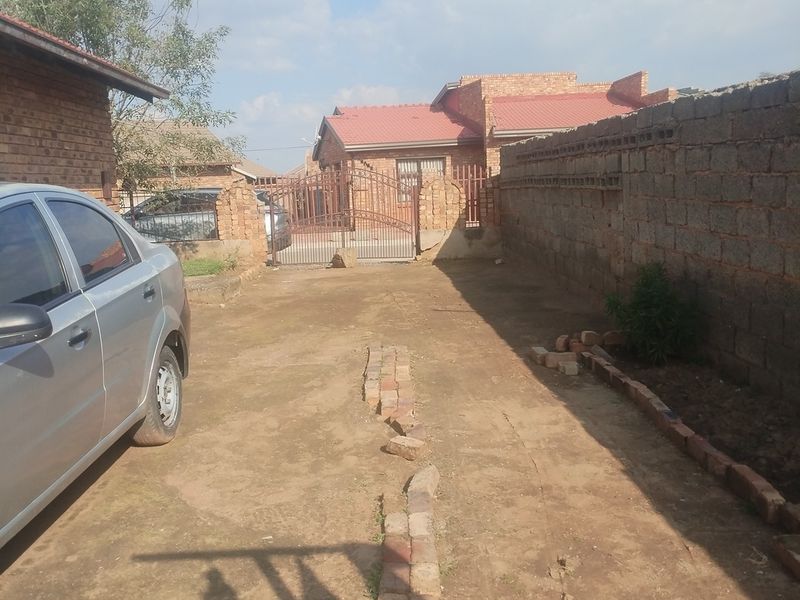 Front exterior view of the property featuring a metal gate, brick boundary wall, and an unpaved driveway area.