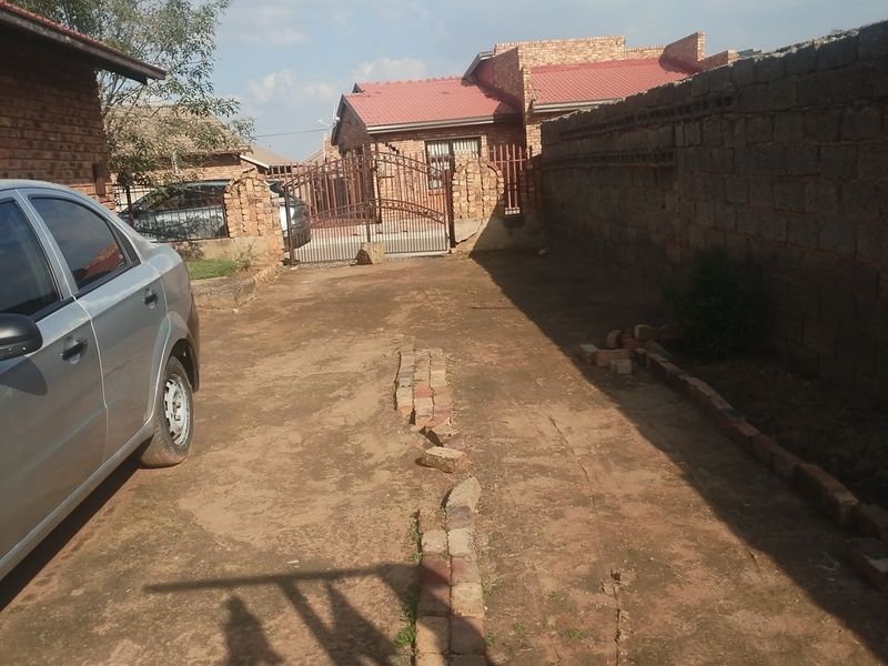 Front exterior view showing a face brick house with a metal gate and an unpaved driveway area.
