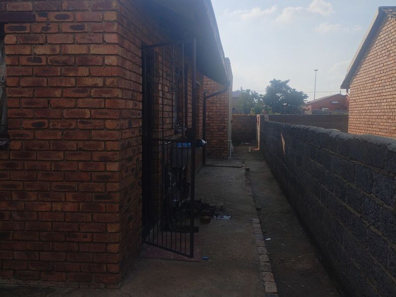 A side exterior view of the property featuring face brick walls, a security gate, and a concrete pathway leading along the boundary wall.