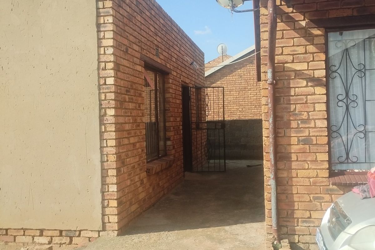 Exterior view of the rear of the property featuring face brick construction, a concrete walkway, and security gate access.