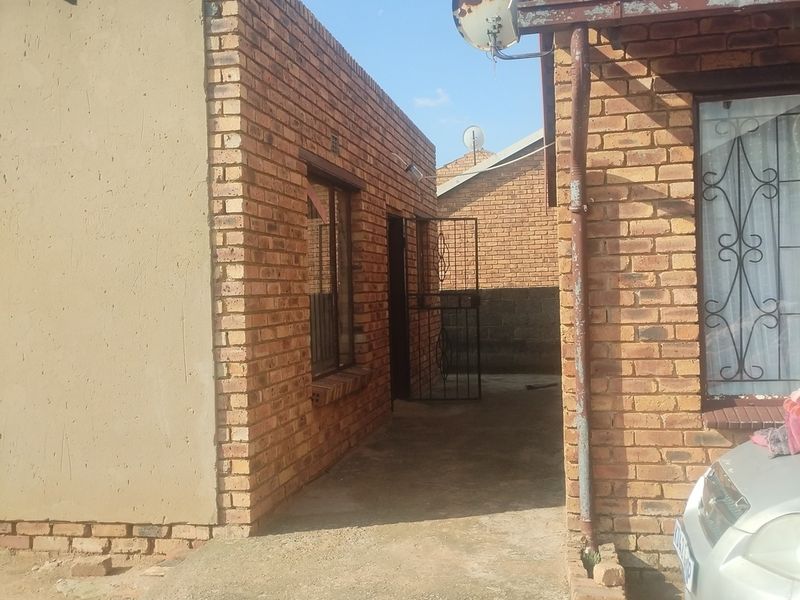 Exterior view of the rear of the property featuring face brick construction, a concrete walkway, and security gate access.