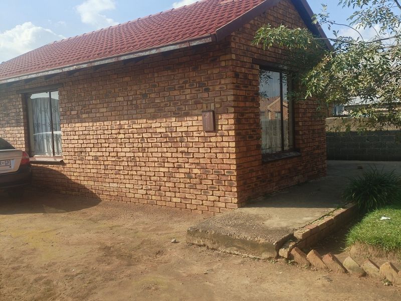 A single-story face brick house featuring a tiled roof, security bars on windows, and a concrete walkway leading to the entrance.