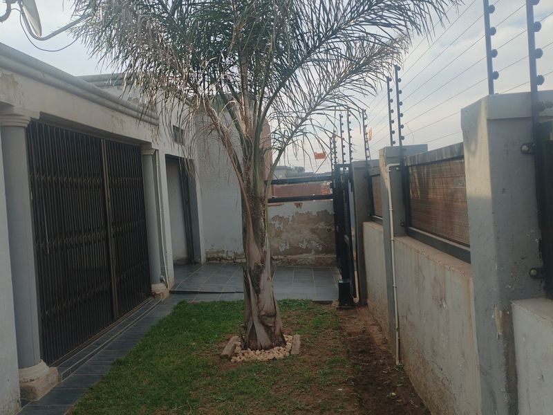 Rear exterior area featuring a small garden, tiled patio, security gate, and perimeter boundary wall with electric fencing.