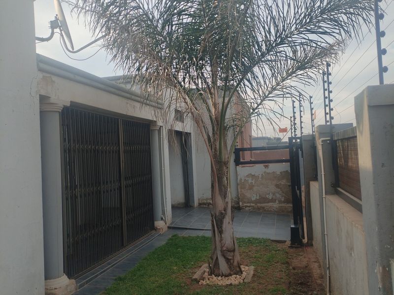 Front exterior view featuring a security gate, tiled patio area, and boundary wall with electric fencing.