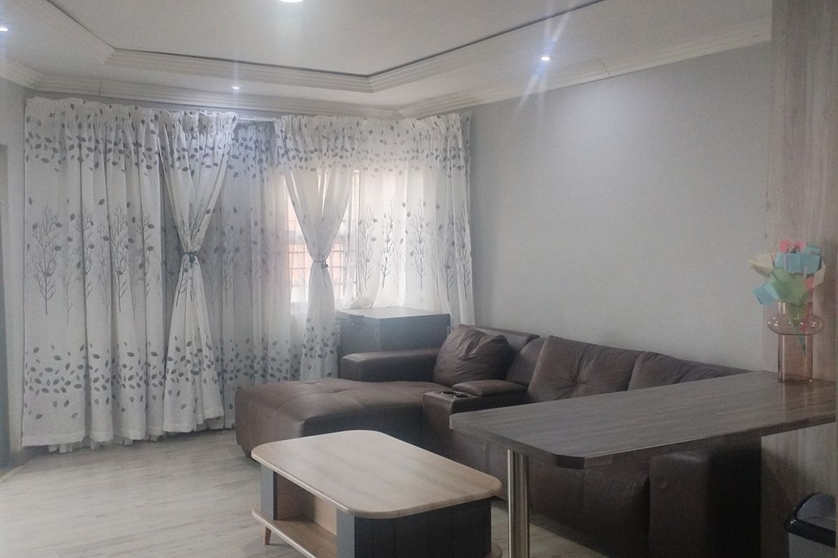 A well-maintained living room featuring recessed ceiling lighting, coved detailing, and light-toned laminate flooring, creating a bright and comfortable living space.