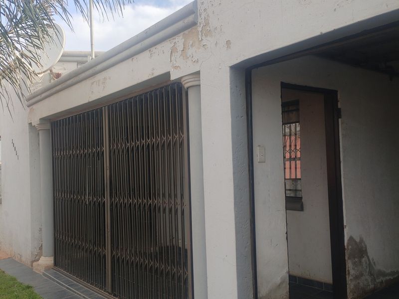 Front exterior view of the property featuring a security gate, tiled entrance area, and visible signs of exterior wall paint deterioration and damp.
