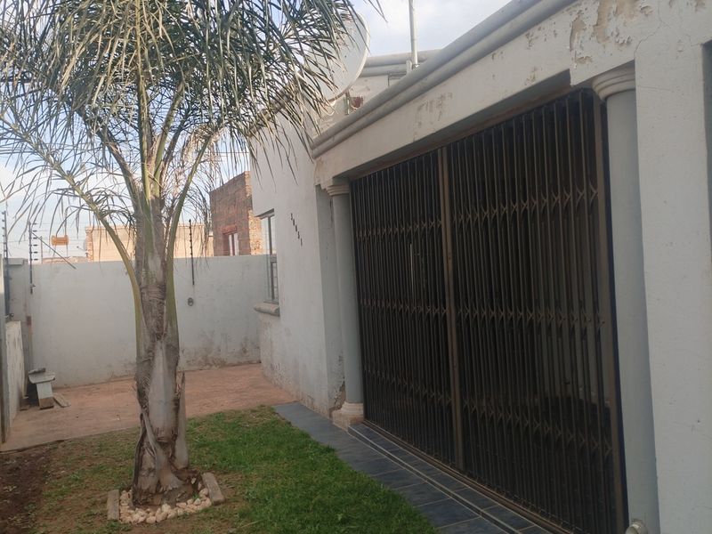 Rear exterior view of the property featuring a tiled patio area, security gate, and a small garden with perimeter wall and electric fencing.