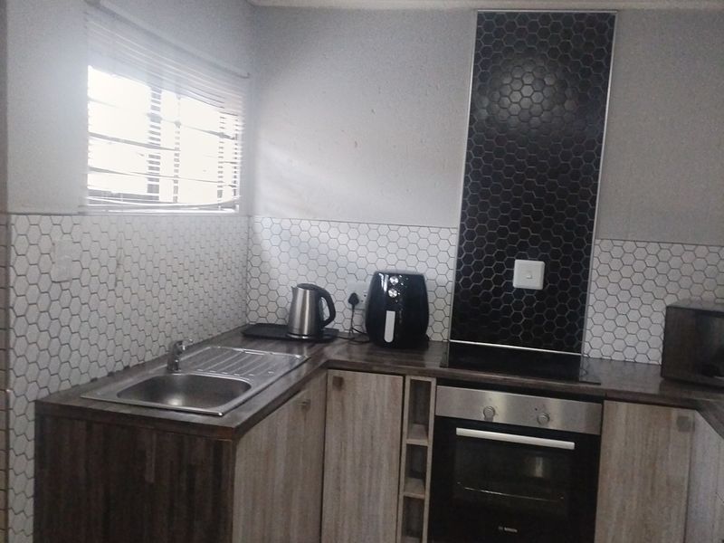 A functional kitchen featuring modern hexagonal tiled backsplashes, built-in oven and hob, stainless steel sink, and wood-finish cabinetry.