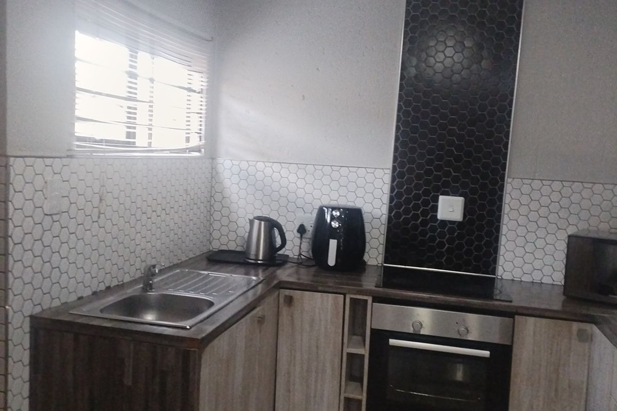 A functional kitchen featuring modern hexagonal tiled backsplashes, built-in oven and hob, stainless steel sink, and wood-finish cabinetry.