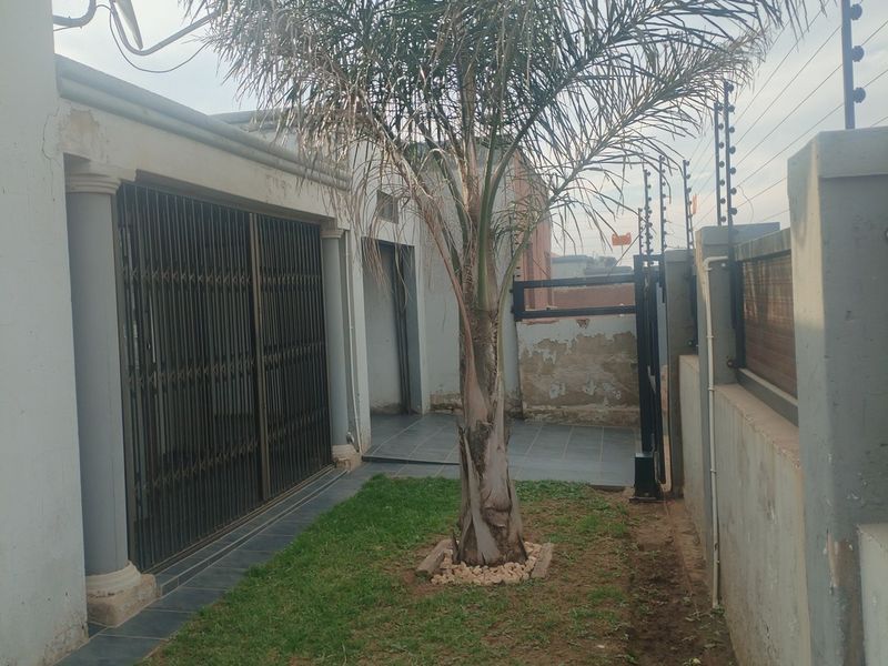 Rear exterior area featuring a small lawn, tiled patio space, security gate, and perimeter electric fencing.