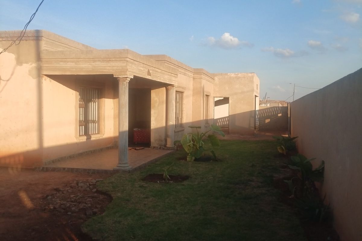 Rear view of the house featuring a covered patio with concrete columns, a small lawn, and a perimeter boundary wall.