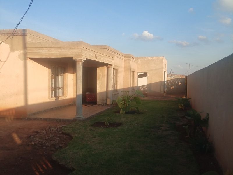 Rear view of the house featuring a covered patio with concrete columns, a small lawn, and a perimeter boundary wall.