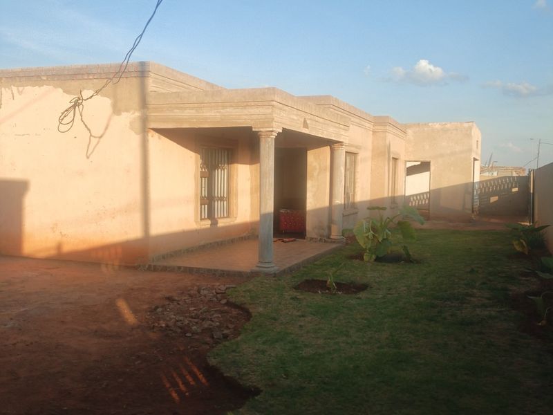Front view of a single-story house featuring a covered porch with concrete columns, currently in an unfinished state with exposed plaster and brickwork.