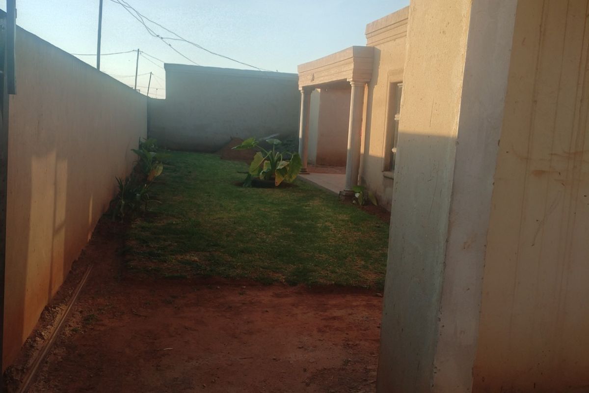 A view of the rear garden area featuring a covered patio with concrete columns and a perimeter boundary wall.
