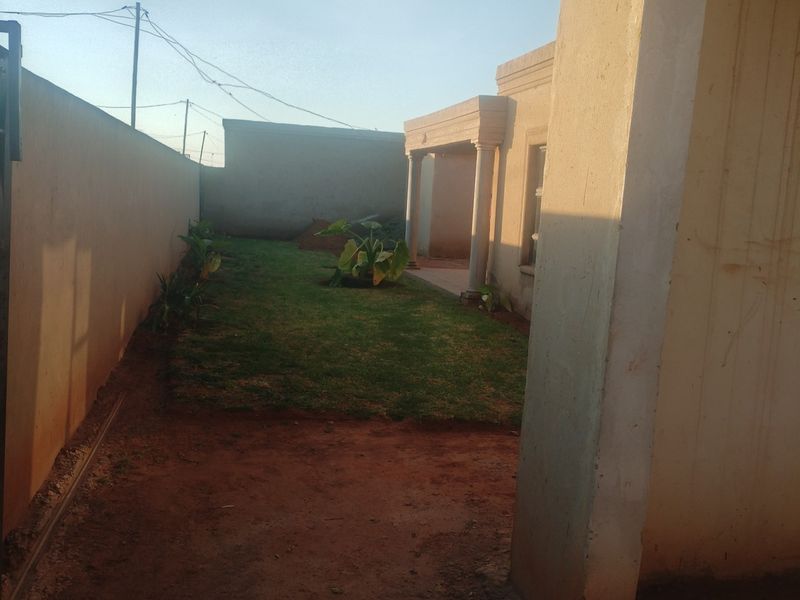 A view of the rear garden area featuring a covered patio with concrete columns and a perimeter boundary wall.