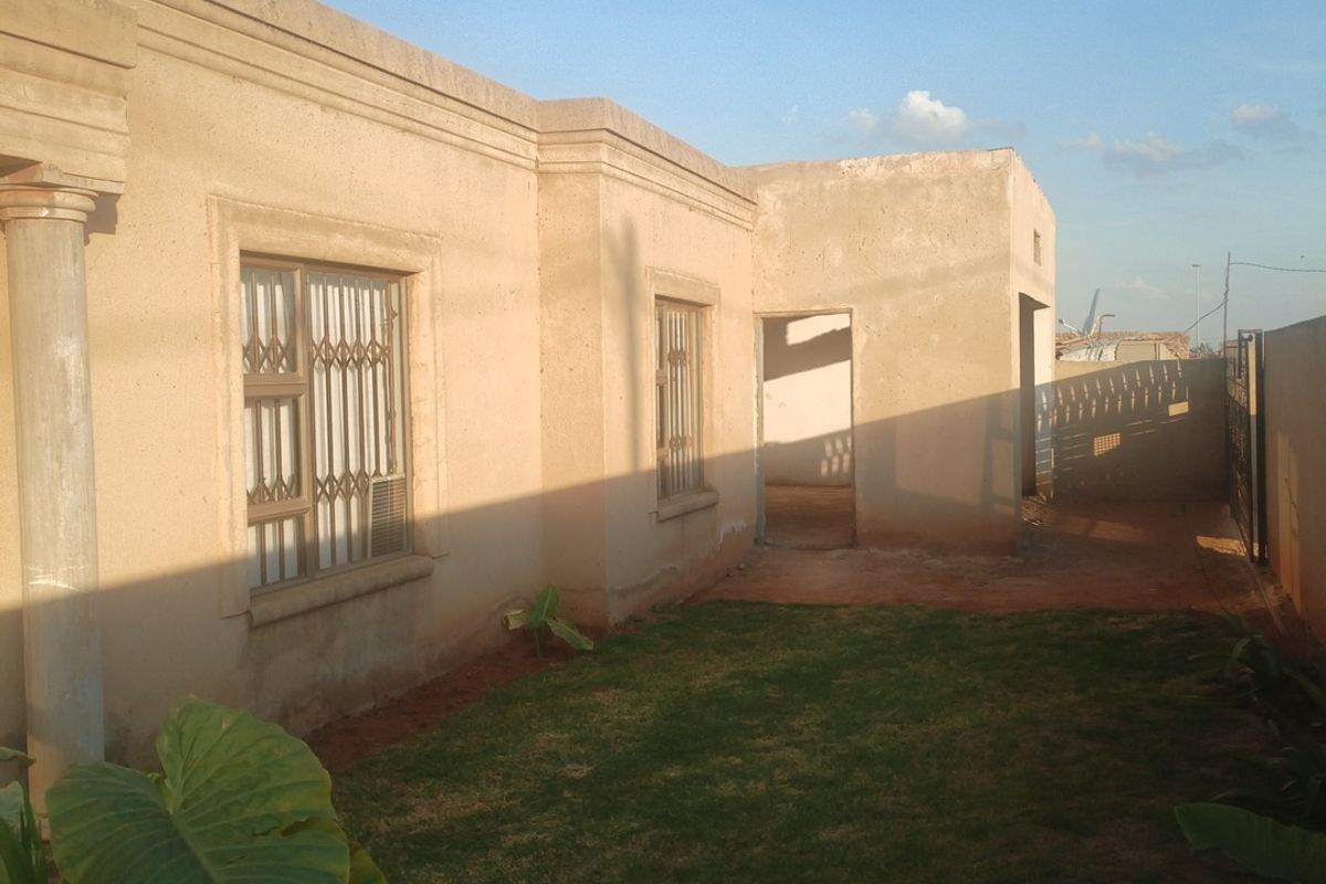 Rear view of the property showing plastered exterior walls, security bars on windows, a concrete column, and a small lawn area.