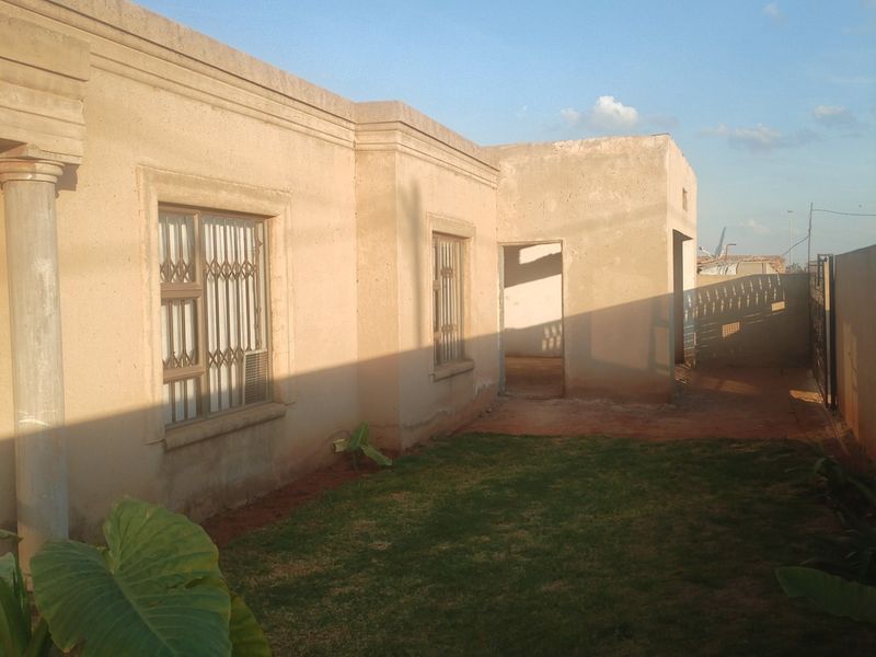 Rear view of the property showing plastered exterior walls, security bars on windows, a concrete column, and a small lawn area.