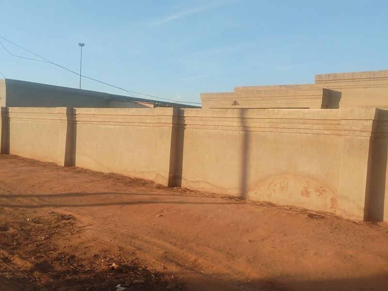 A view of the property's exterior perimeter wall featuring concrete construction along an unpaved road.