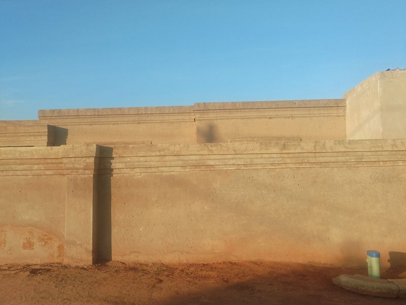 A view of the property's exterior boundary wall featuring concrete coping and a natural earth ground surface.