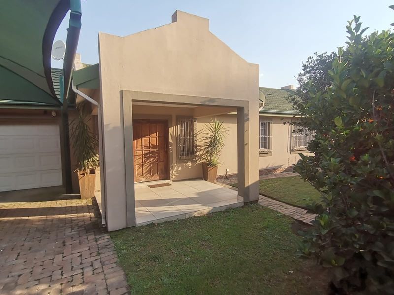 Front entrance of the house featuring a covered tiled porch, wooden front door, security window bars, and paved driveway access.