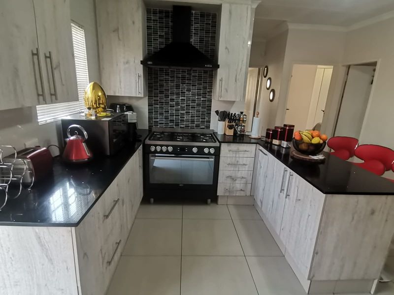 A modern kitchen featuring light wood-grain cabinetry, contrasting black granite countertops, a gas stove with an extractor fan, and a stylish mosaic tiled backsplash.