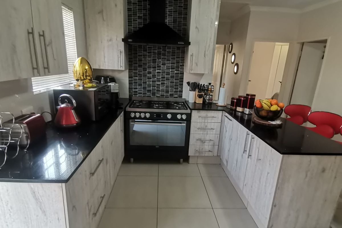 A modern kitchen featuring light wood-grain cabinetry, contrasting black granite countertops, a gas stove with an extractor fan, and a stylish mosaic tiled backsplash.