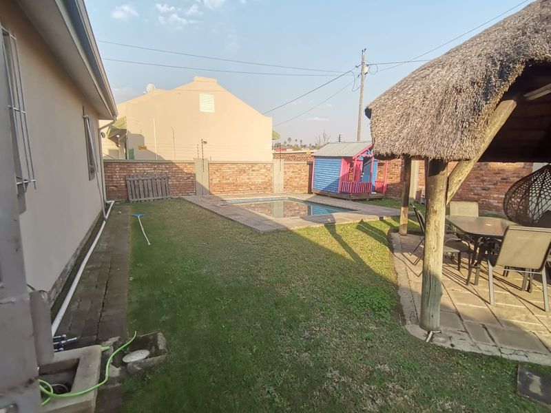 Rear garden featuring a swimming pool, a thatched lapa, and a paved patio area enclosed by a brick boundary wall.